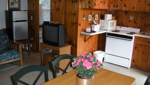 Una cocina compacta con armarios de madera, un refrigerador, un microondas y una estufa. Hay una mesa de comedor con sillas y una pequeña planta en maceta.
