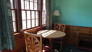 Una habitación con una mesa y sillas de madera, una lámpara y una ventana con cortinas.