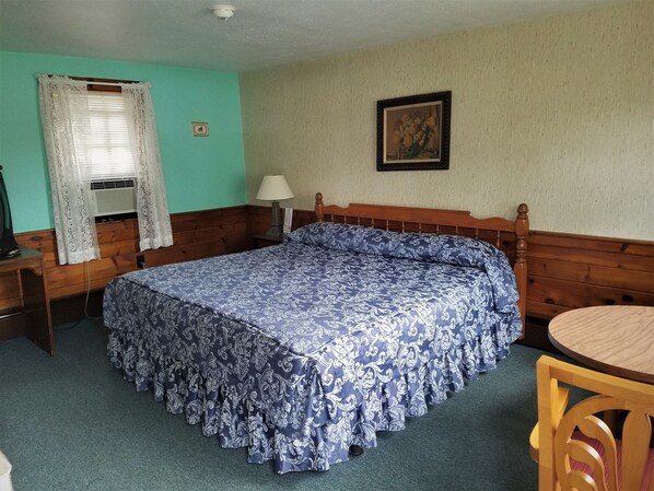 Una habitación con cama, escritorio, silla, lámpara y un cuadro en la pared.