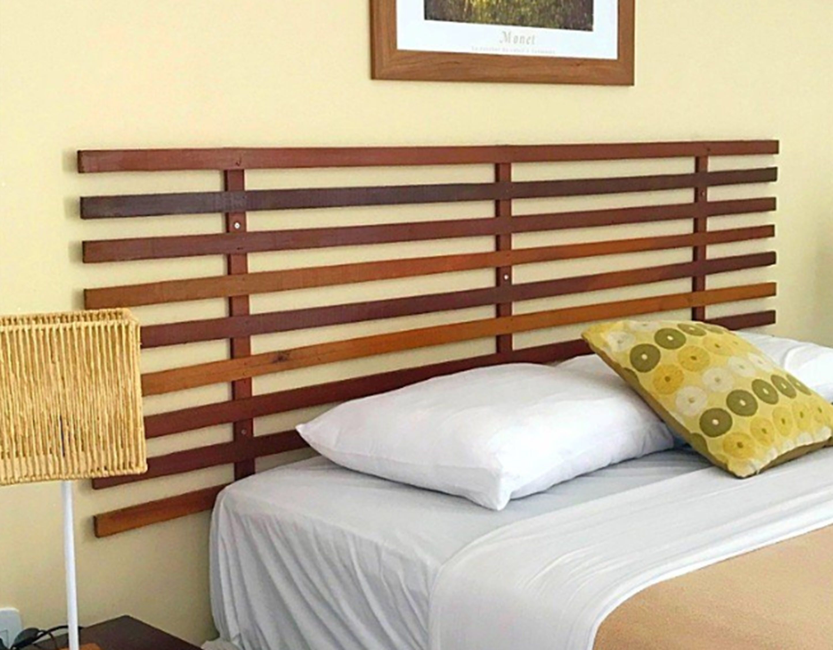 A bed with a wooden slat headboard, white bedding, and a yellow patterned pillow.