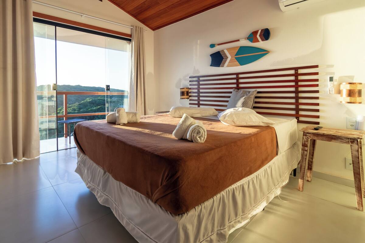 Ein Schlafzimmer mit einem großen Bett, einem Holzkopfende, einem Nachttisch und Blick durch eine Schiebetür.