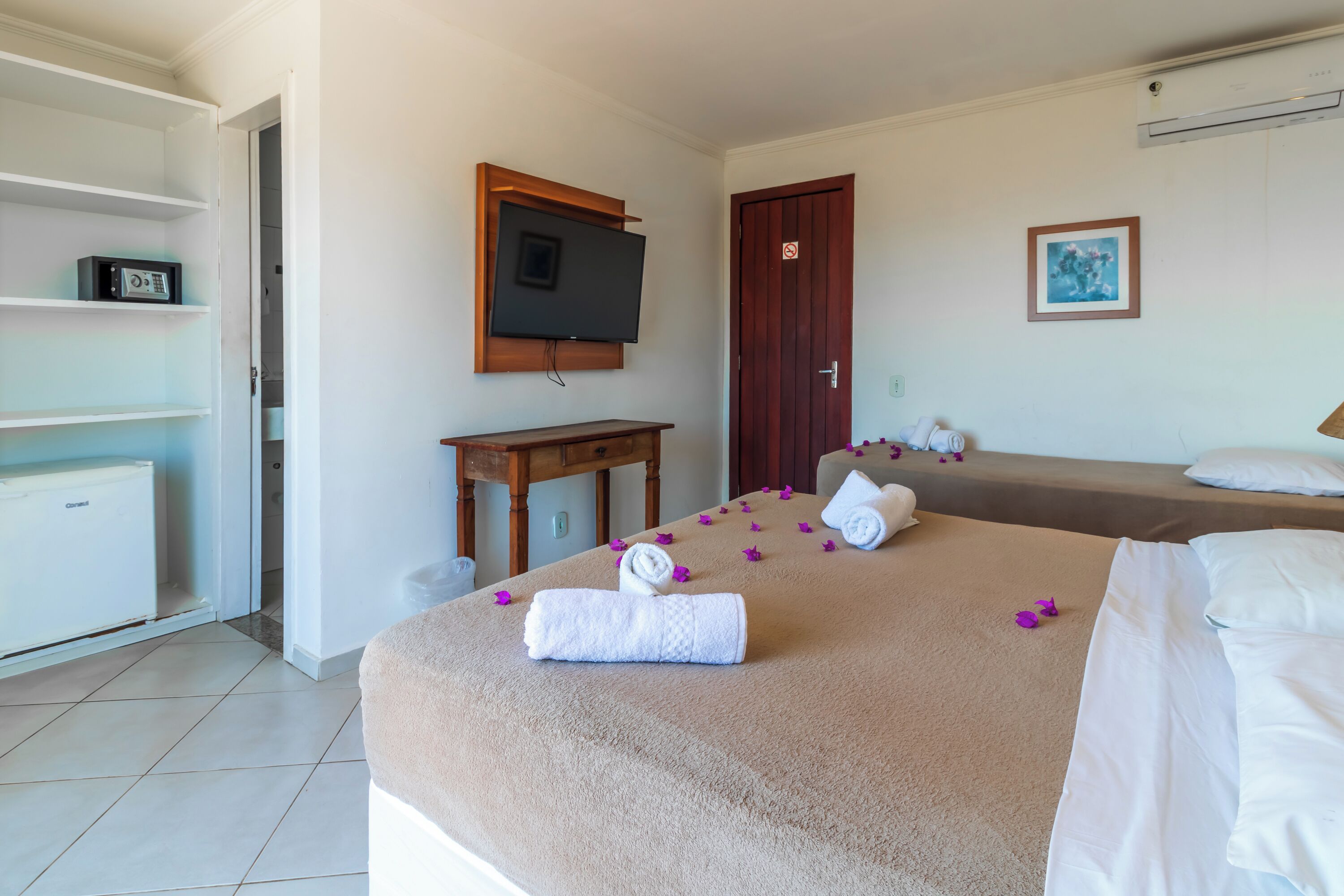 Una habitación de hotel con cama, televisión en la pared, escritorio de madera y armario.
