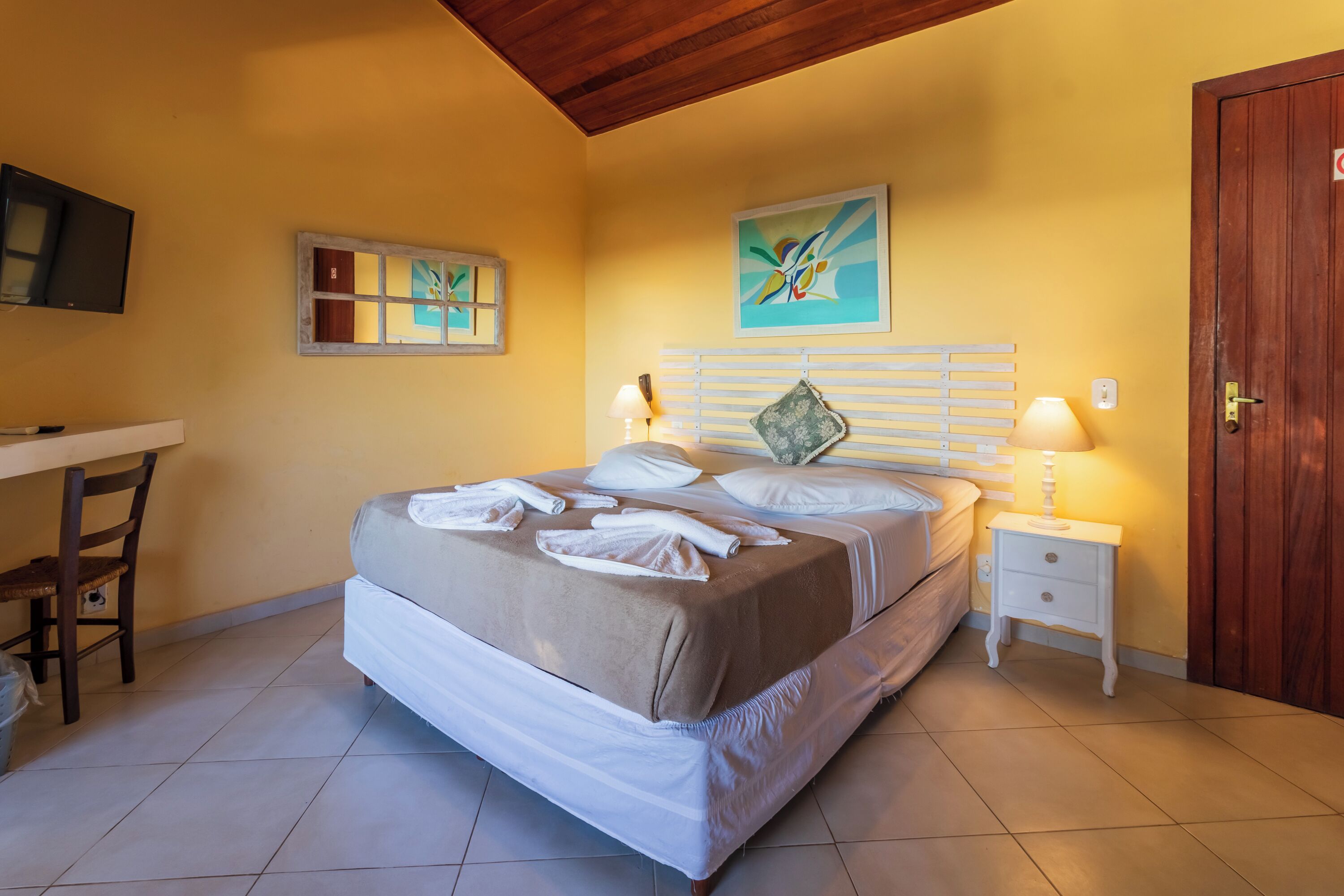 A hotel room with a bed, bedside tables, a desk, and artwork on the walls.