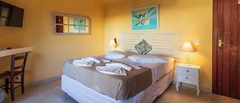 A hotel room with a bed, bedside tables, a desk, and artwork on the walls.
