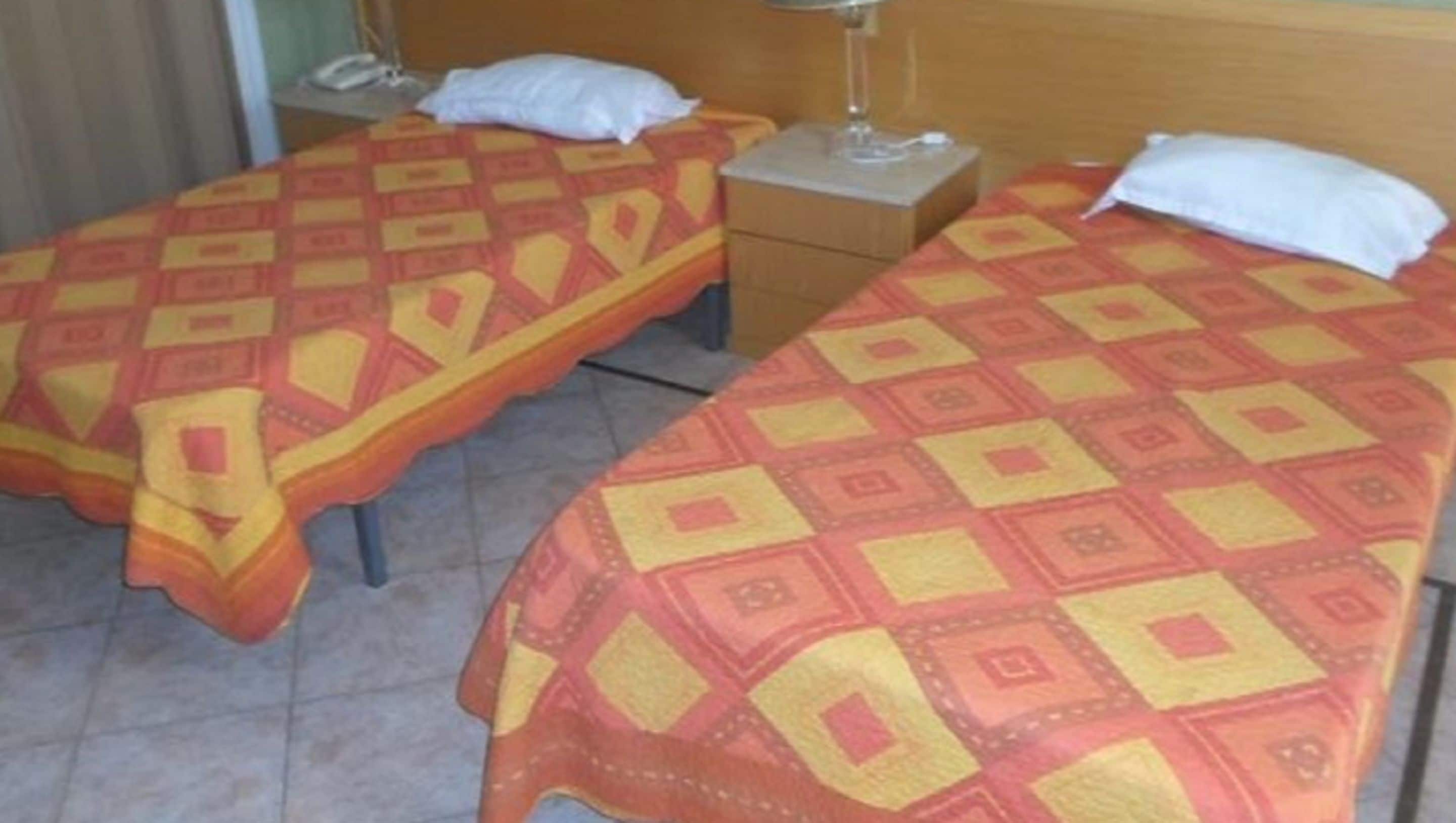 Two single beds with patterned bedding, bedside tables with lamps, and a wooden headboard.