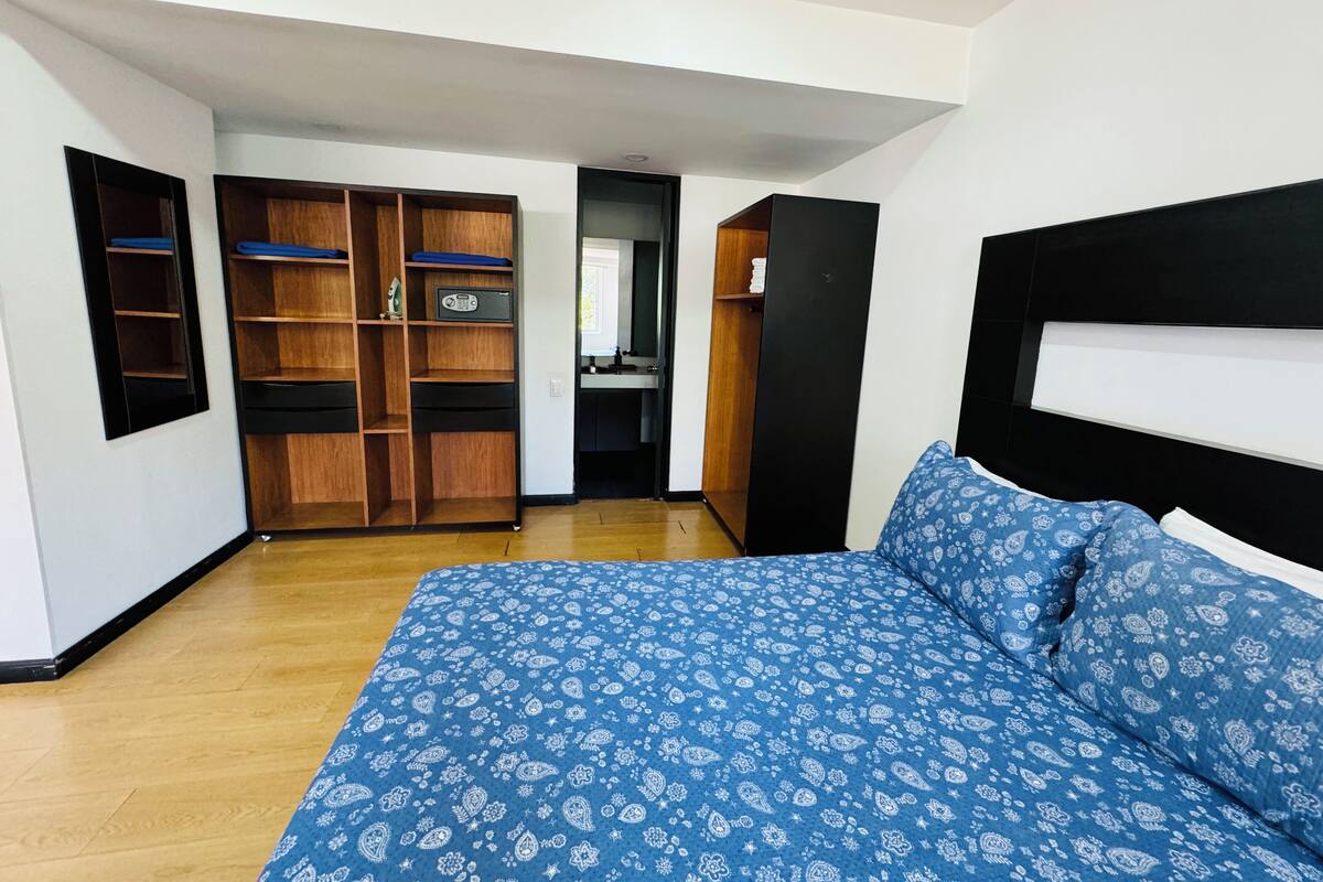 A bedroom with a bed, wooden wardrobe, and a mirror.