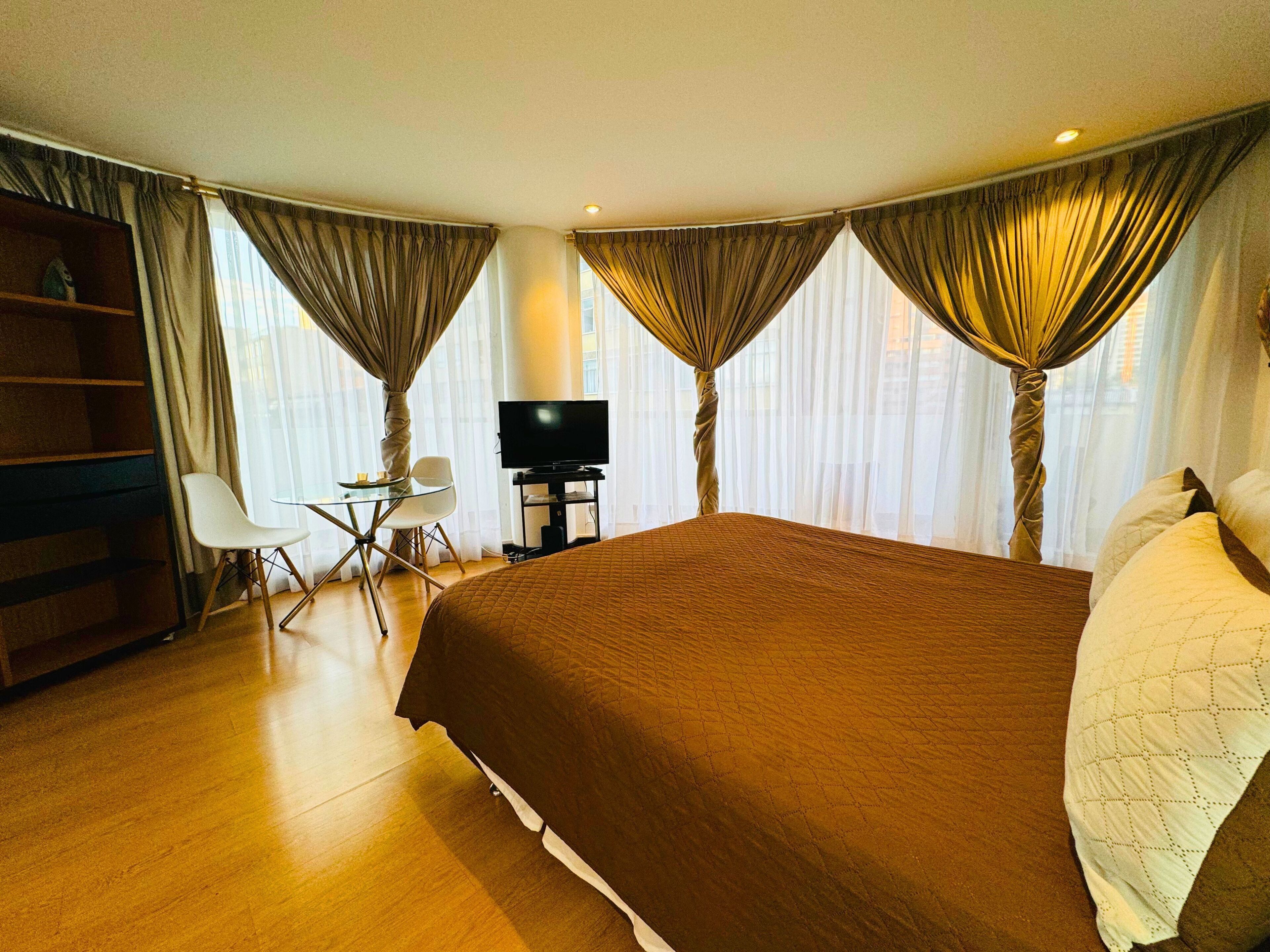 A hotel room with a large bed, a desk with a chair, a television, and a bookshelf.