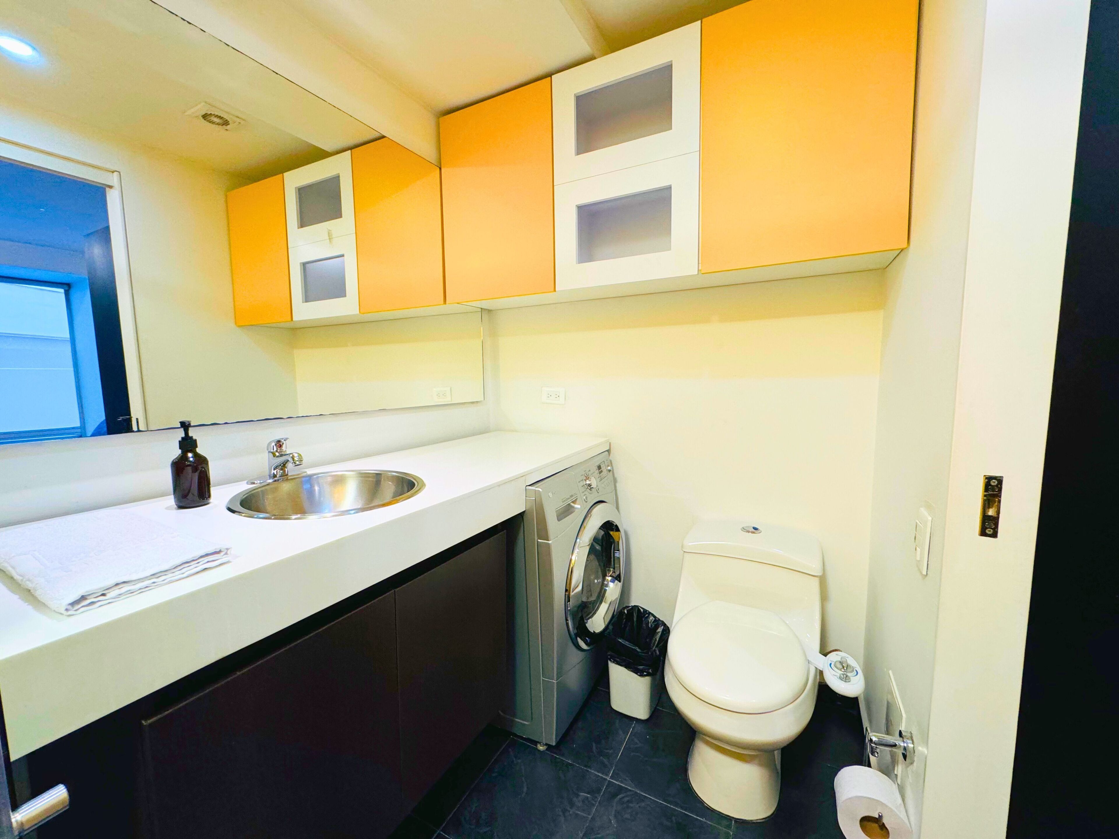 A compact kitchen with a sink, washing machine, and toilet.