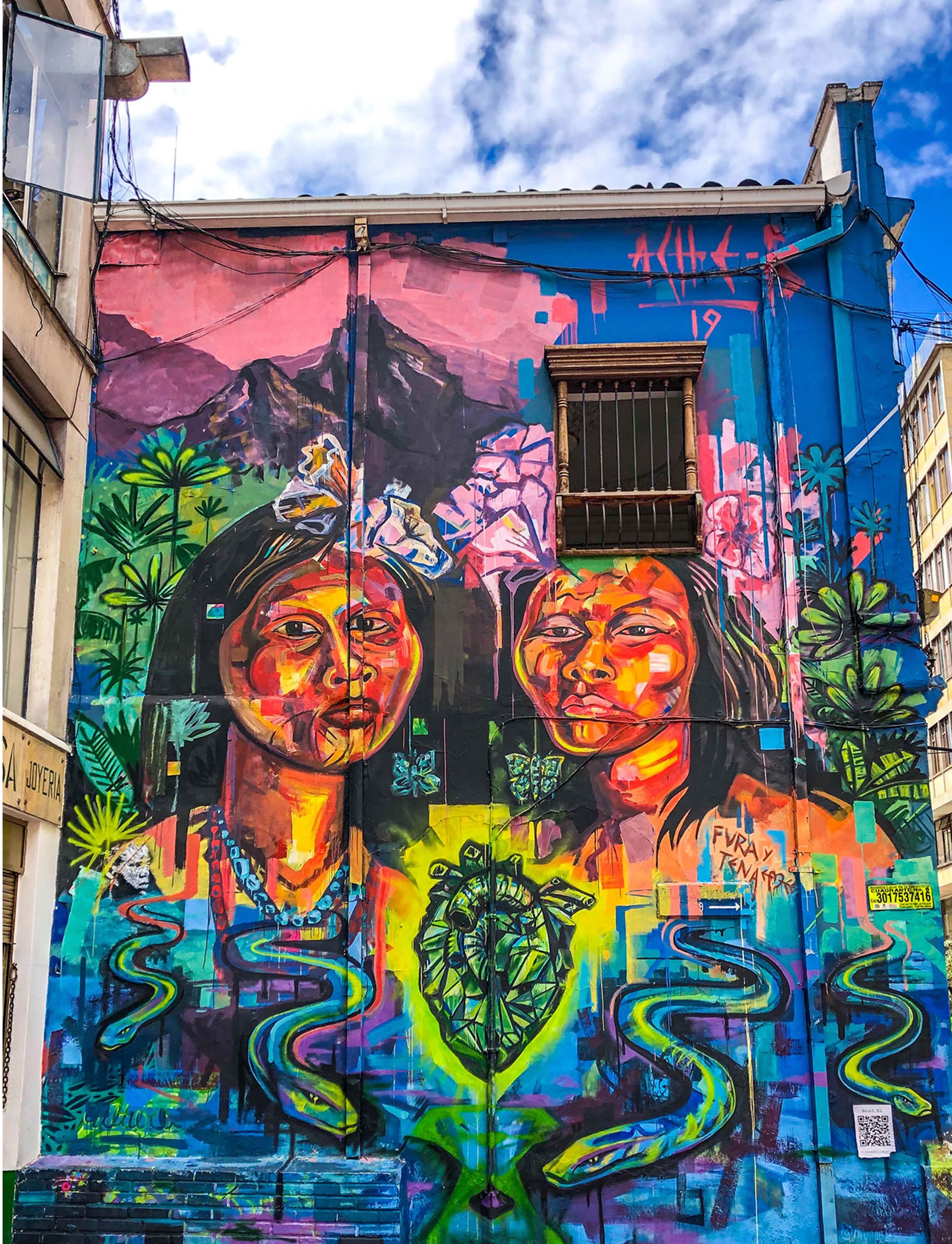A vibrant mural on a building's exterior featuring abstract faces, floral patterns, and a window.