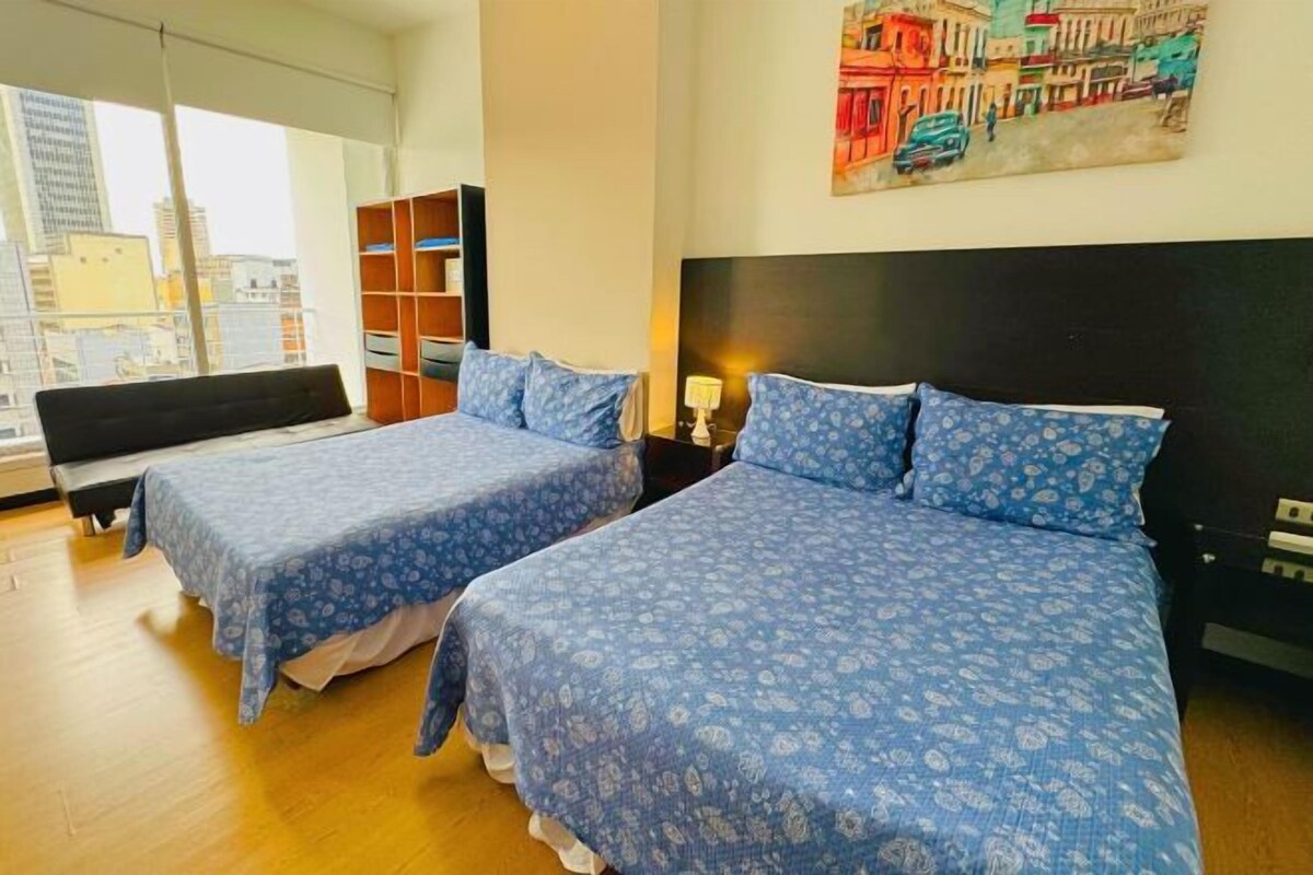 Habitación de hotel con dos camas, vista a la ciudad, una estantería y un cuadro en la pared.