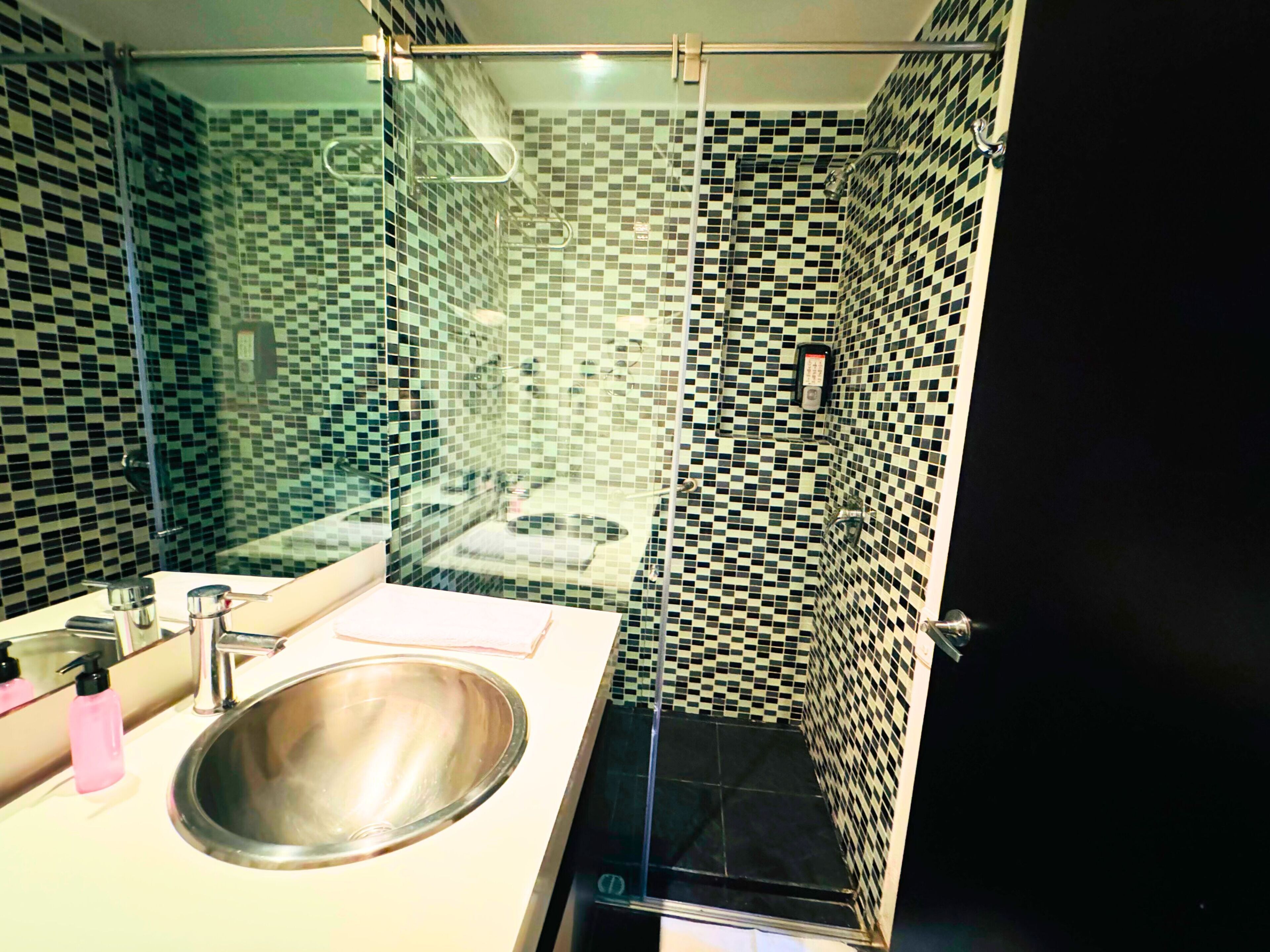 A modern bathroom with a glass shower enclosure, a sink with a mirror, and a tiled floor.