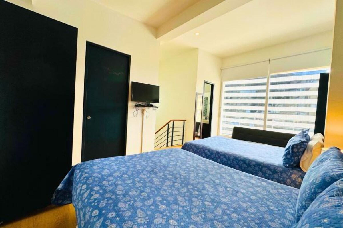 A bedroom with two beds, a TV, and a window with blinds.
