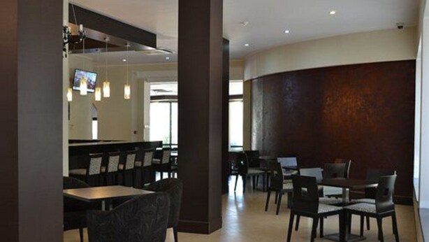 A modern dining area with tables and chairs, a television mounted on the wall, and a large wooden accent wall. - Jardy Hôtel & Suites (Algiers)
