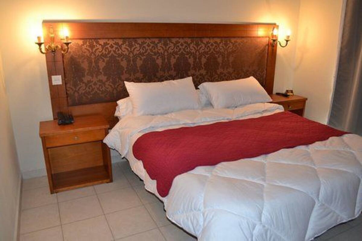 A neatly made bed with a red blanket, wooden headboard with a patterned design, and bedside lamps.