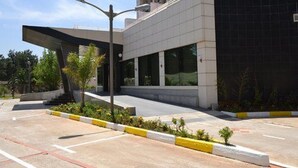 A modern building with a covered entrance, a parking lot with marked spaces, and a landscaped area with small plants. - Jardy Hôtel & Suites (Algiers)