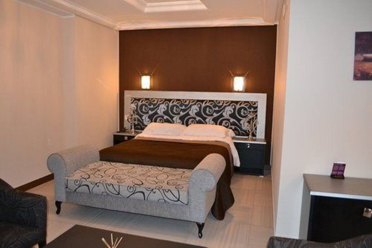 A neatly arranged hotel room with a bed, a nightstand, a small table, and a sofa.
