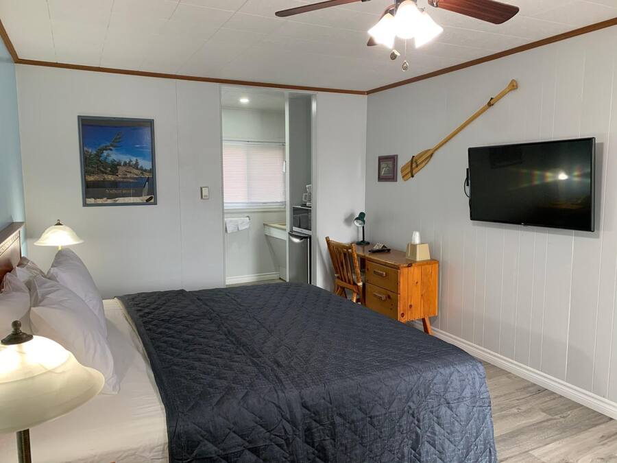 Un dormitorio con cama, escritorio, silla, televisor y ventilador de techo.