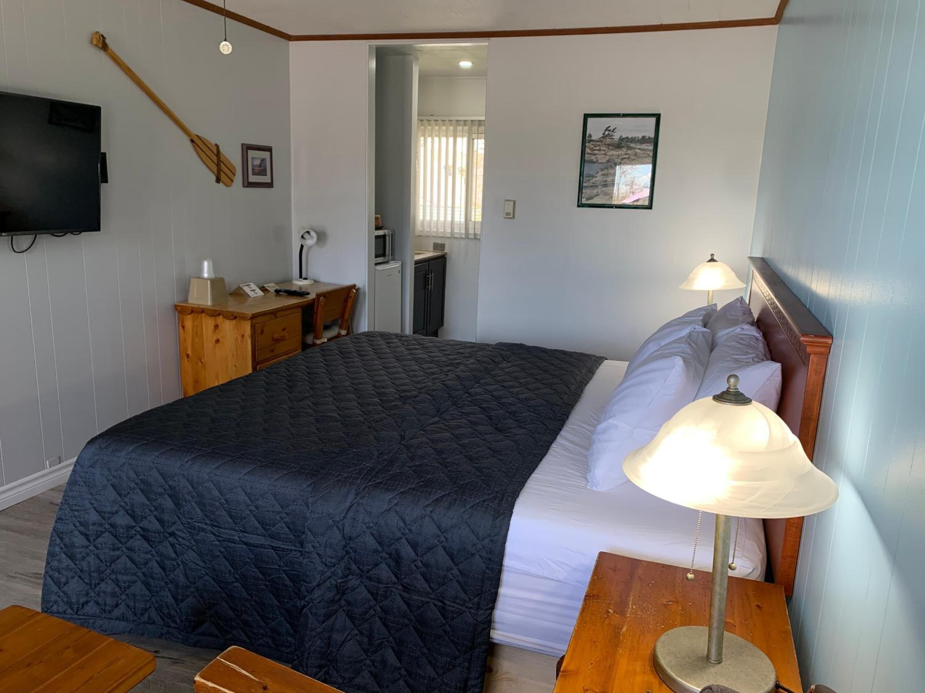 Ein Schlafzimmer mit Bett, Nachttischlampe, Holzschreibtisch, Stuhl und Fernseher an der Wand.