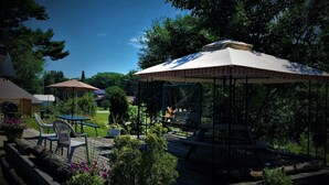 A gazebo with a roof, surrounded by a wooden deck, and a table with chairs. - Town and Country Motel (Parry Sound)