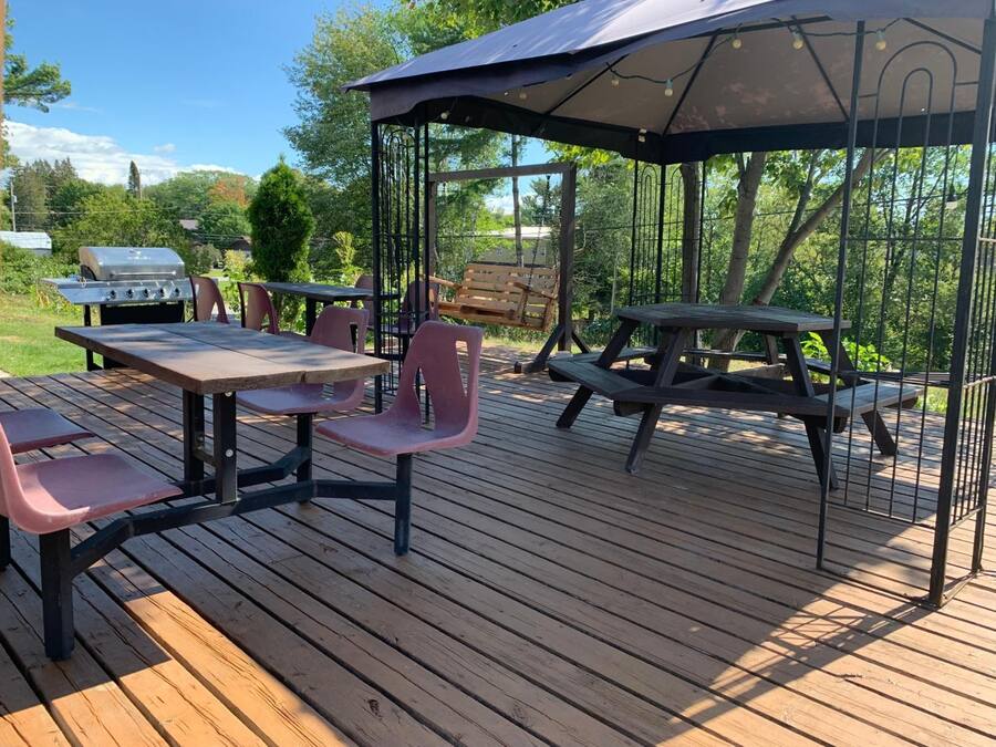 Une terrasse en bois avec des tables et des chaises pour pique-niquer, un espace de repos couvert et un barbecue.