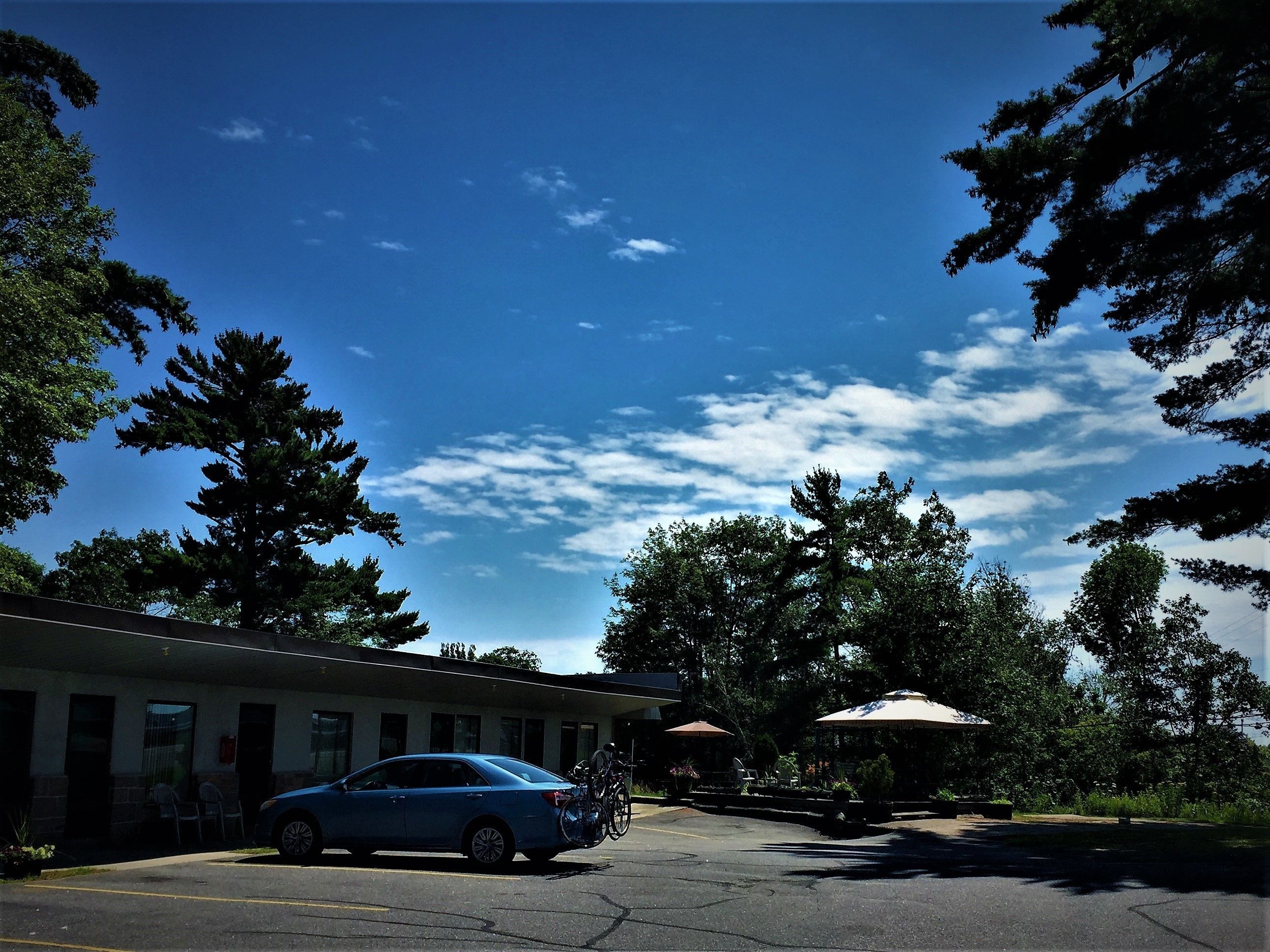 A motel with a blue car parked in front, surrounded by trees and a clear sky.