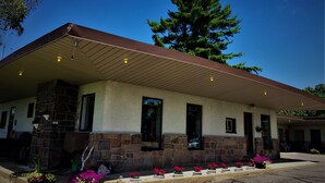 A building with a stone facade, a covered patio area, and a large tree in the background. - Town and Country Motel (Parry Sound)
