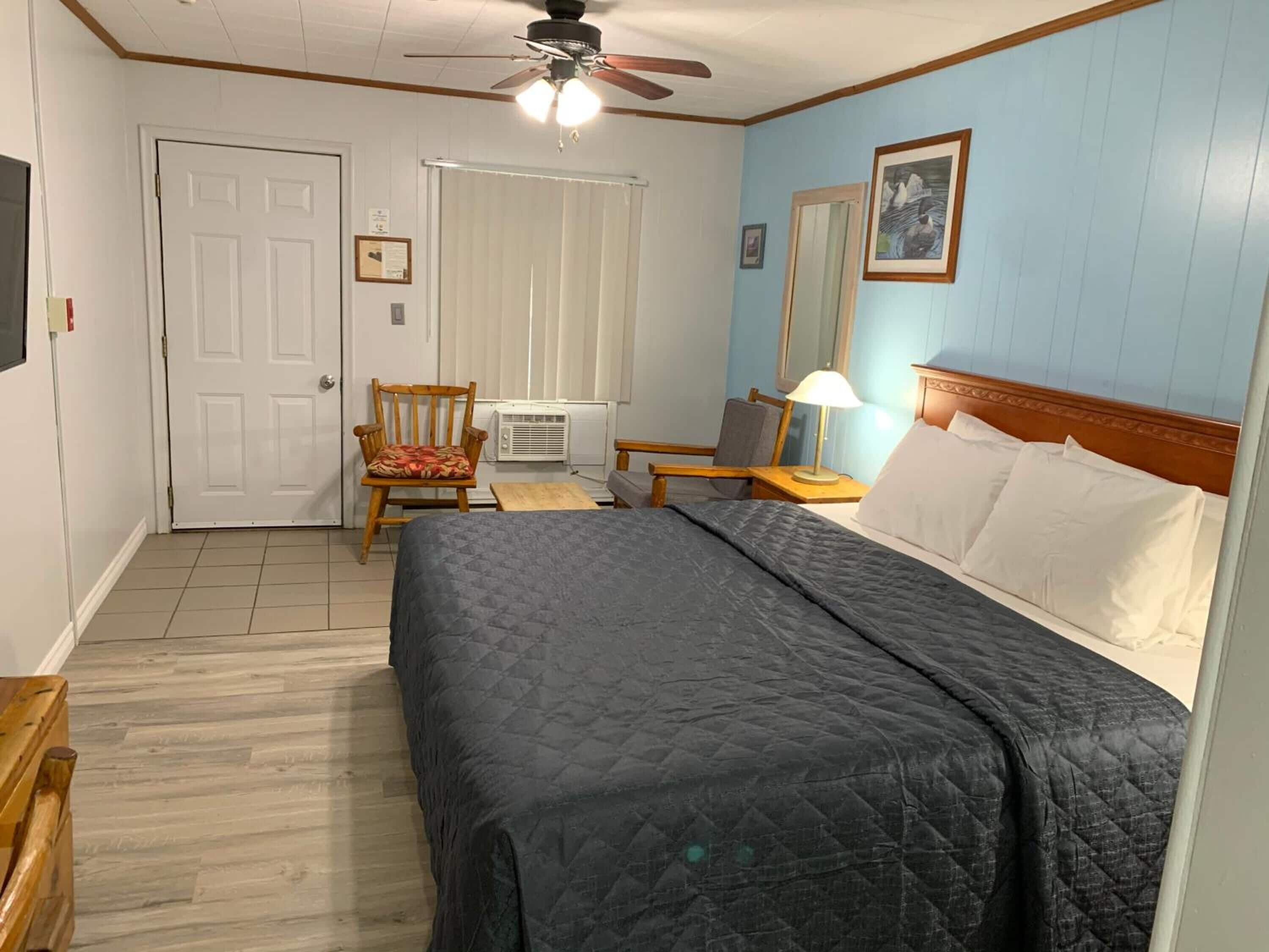 Une chambre à coucher comprenant un lit, une chaise, un bureau, un ventilateur de plafond et une fenêtre avec des stores.