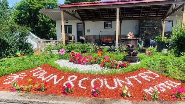 A garden area with a pathway leading to a building with a red roof and stone walls. - Town and Country Motel (Parry Sound)