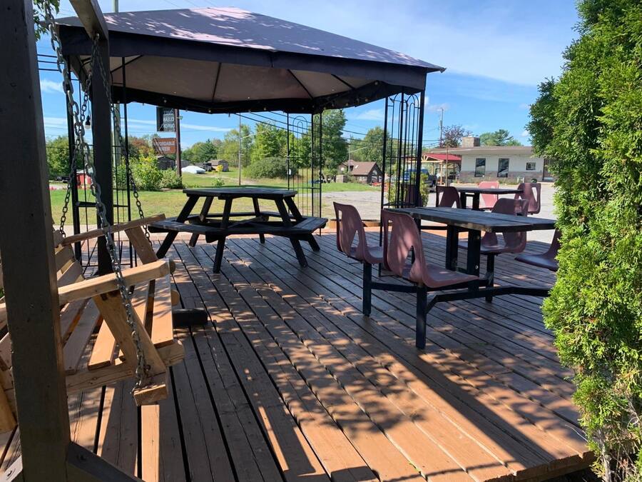Une terrasse extérieure en bois, avec des tables et des chaises pour pique-nique, une balançoire et un espace de repos abrité.