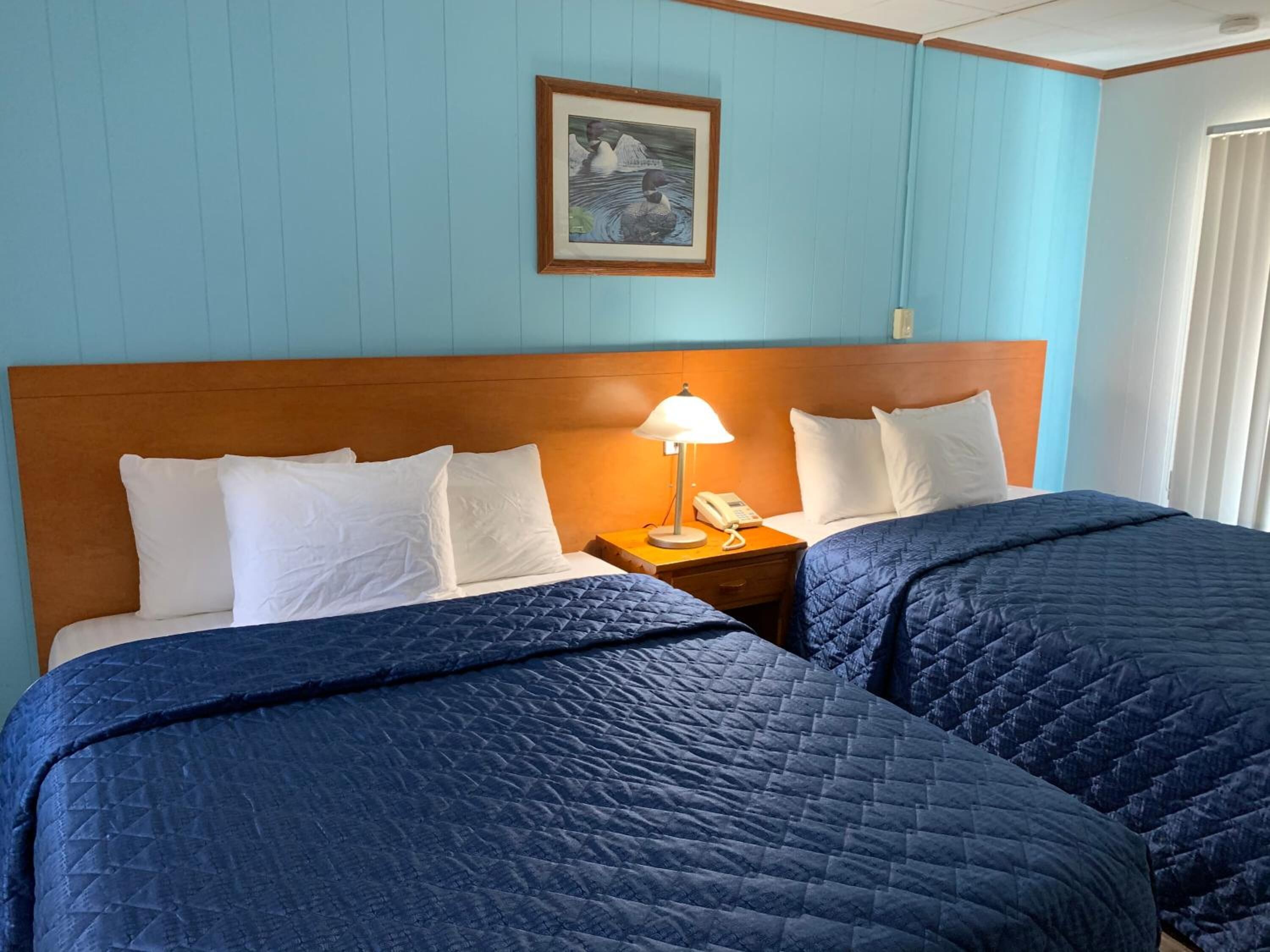 Ett hotellrum med två sängar, en sänggavel i trä, ett nattduksbord med en lampa och en inramad tavla på väggen.
