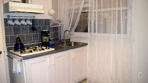 A kitchen with white cabinets, a gas stove, a sink, and a window with sheer curtains.