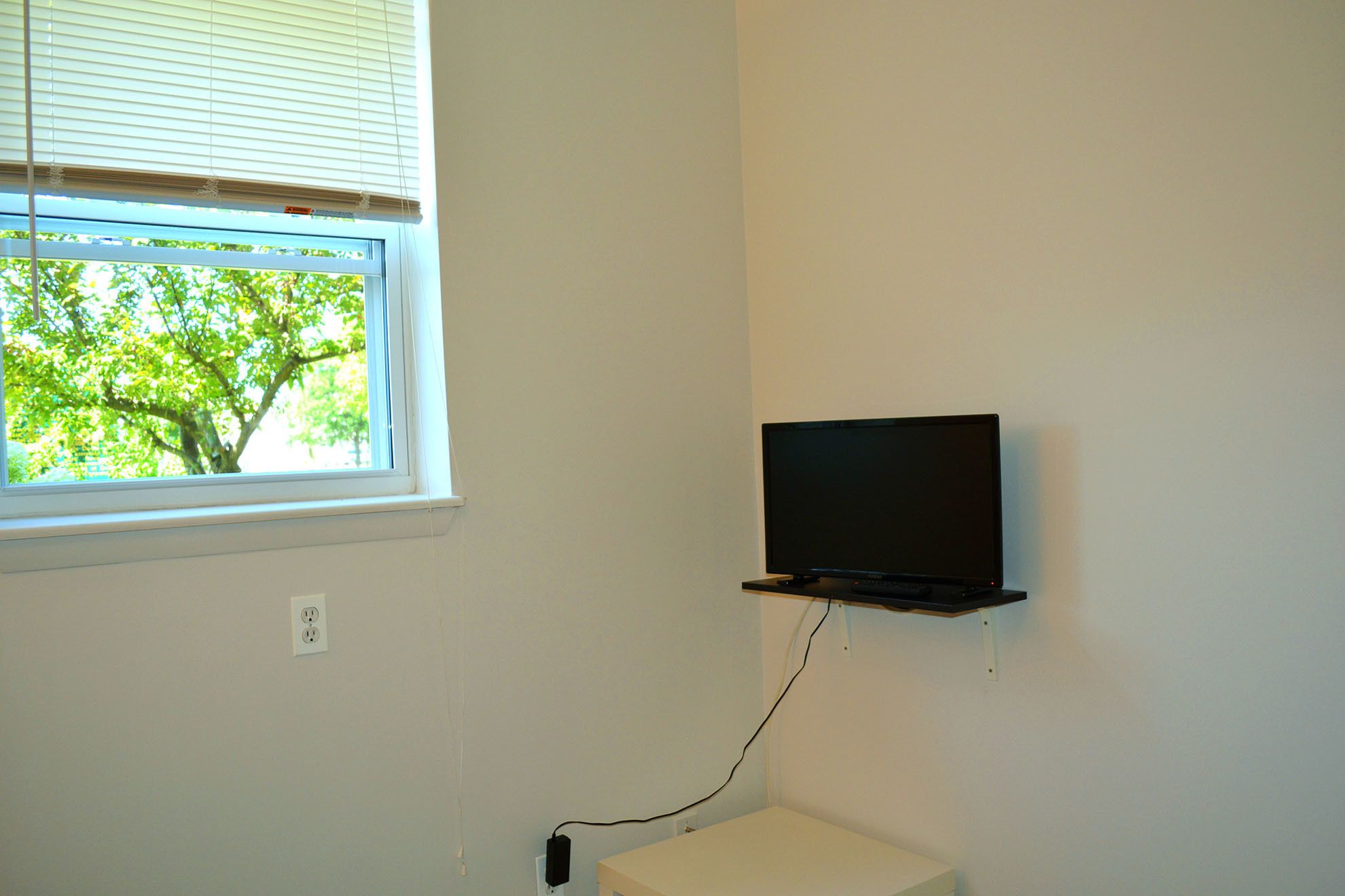 A room with a window, a wall-mounted TV, and a power outlet.