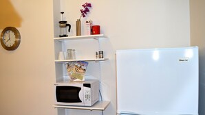 A kitchen with a white refrigerator, a microwave on a shelf, and a clock on the wall.