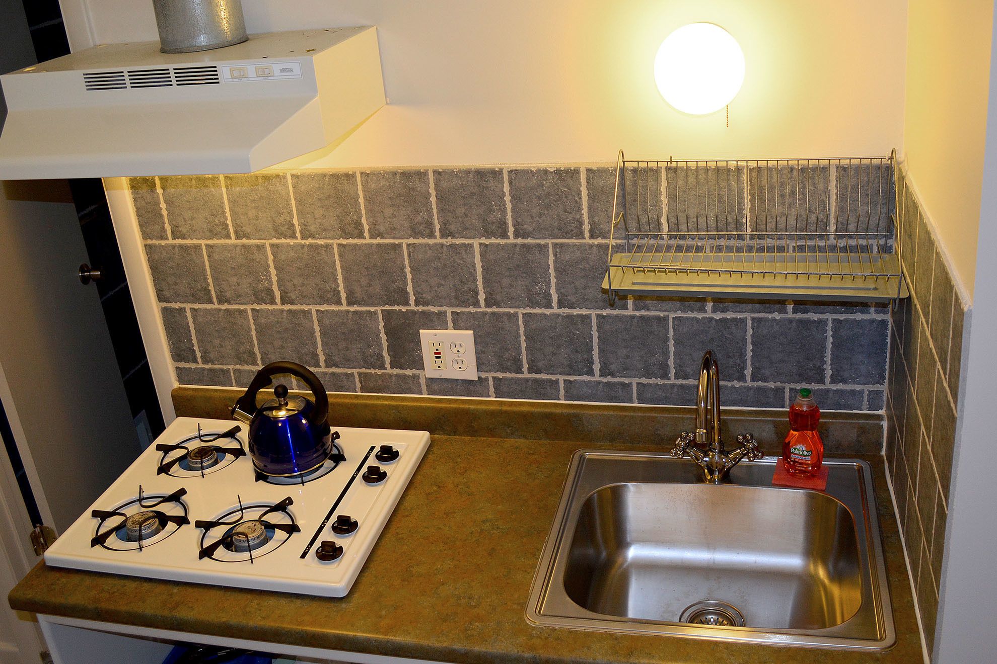 Una cocina con estufa a gas, hervidor, pileta y salpicadero de azulejos.