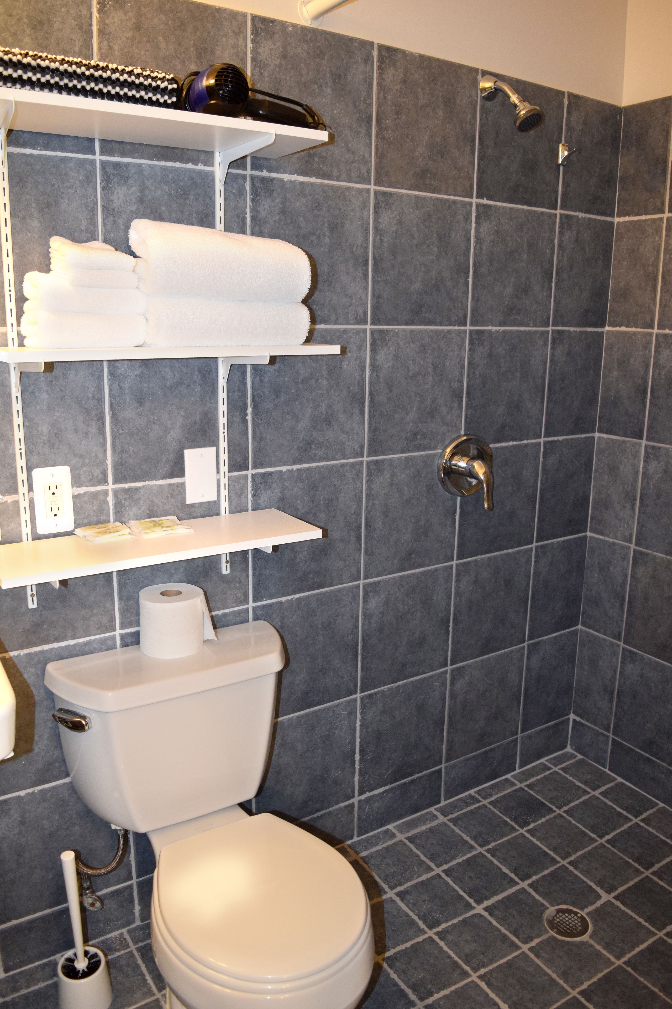 A bathroom with a toilet, a shower, and shelves with towels and toiletries.