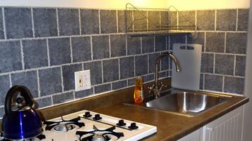 A compact kitchen with a gas stove, a kettle, a sink, and a backsplash of gray tiles.