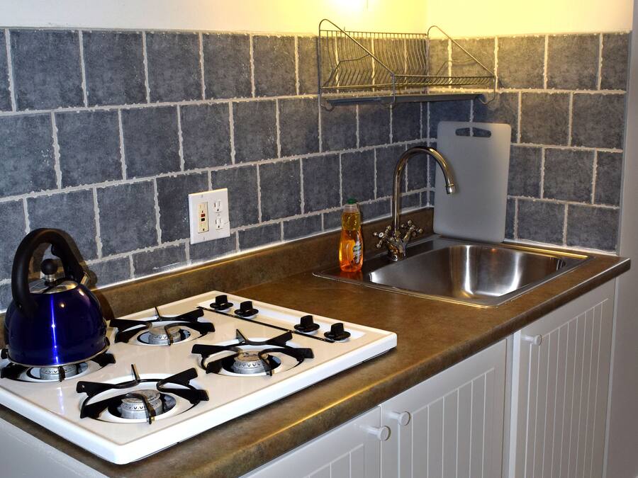 A compact kitchen with a gas stove, a kettle, a sink, and a backsplash of gray tiles.