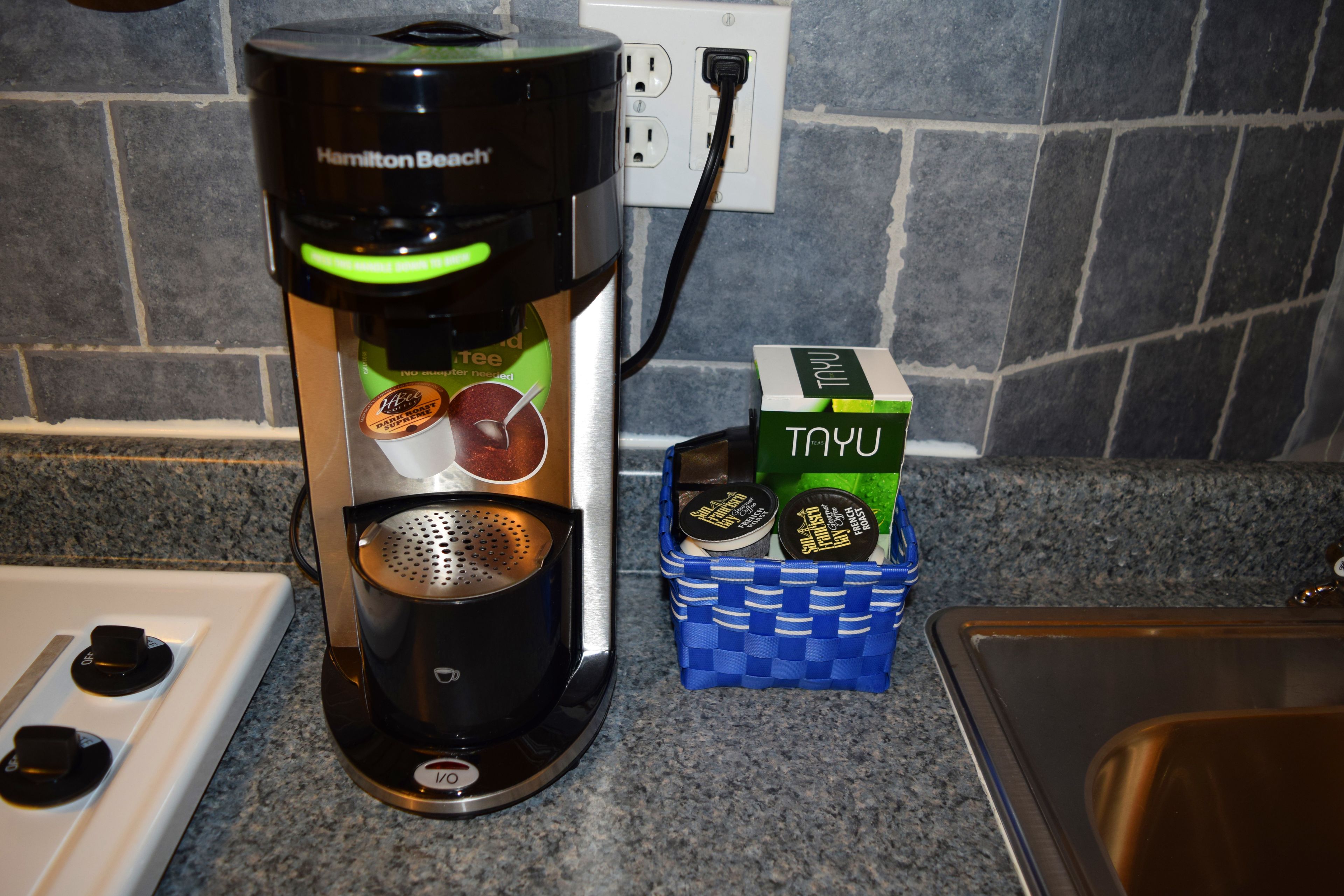 A Hamilton Beach coffee maker on a kitchen counter next to a basket of coffee pods.