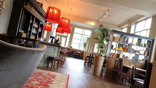 A spacious hotel lobby with a bar, a library, and a seating area. - The Station Hotel (London)