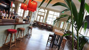 A bar area with wooden stools, a bar counter with beer taps, and large windows allowing natural light. - The Station Hotel (London)