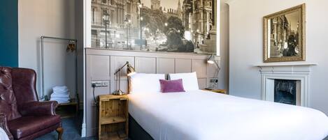 A hotel room with a large bed, a red armchair, a wooden nightstand, a mirror, and a fireplace.