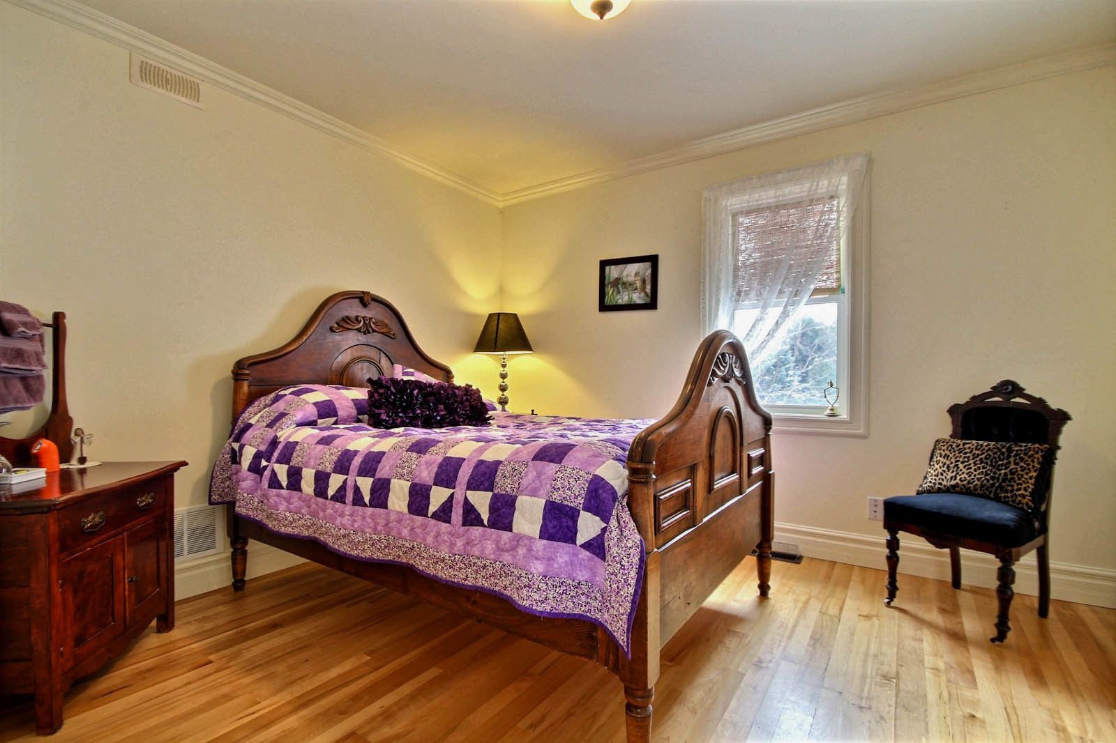 A bedroom with a wooden bed, a nightstand, a chair, and a window with blinds.