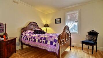 A bedroom with a wooden bed, a nightstand, a chair, and a window with blinds.