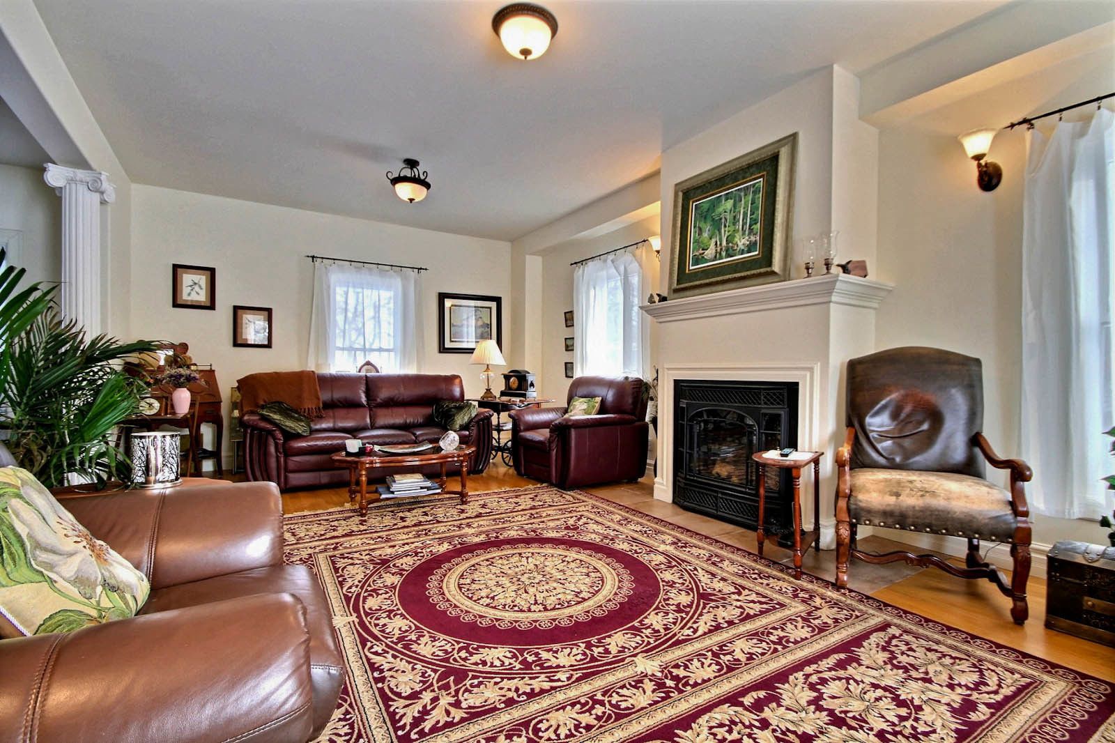 A spacious living room with a fireplace, leather sofas, a patterned rug, and a large window allowing natural light.