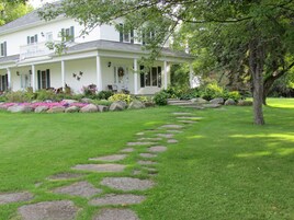 A white house with a porch, surrounded by a well-maintained lawn and a stone pathway leading to the entrance.