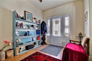 A cozy room with a bookshelf, a red bedspread, a wooden chair, and a door with curtains. - Terrace Green Bed & Breakfast (North Dundas)