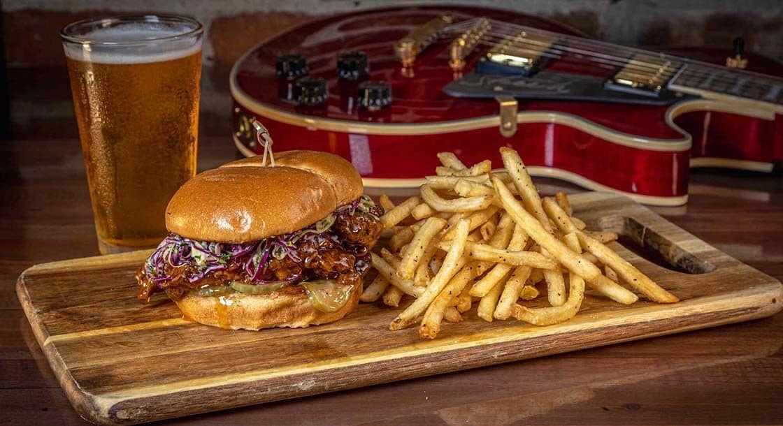 A burger with fries and a glass of beer on a wooden board.