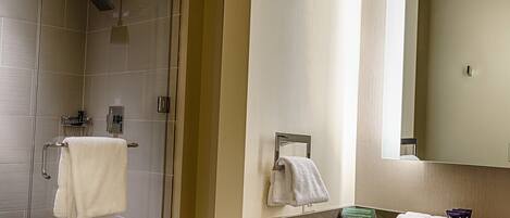 Une salle de bain moderne avec une douche à parois de verre, un meuble-lavabo avec un miroir et des serviettes soigneusement pliées.