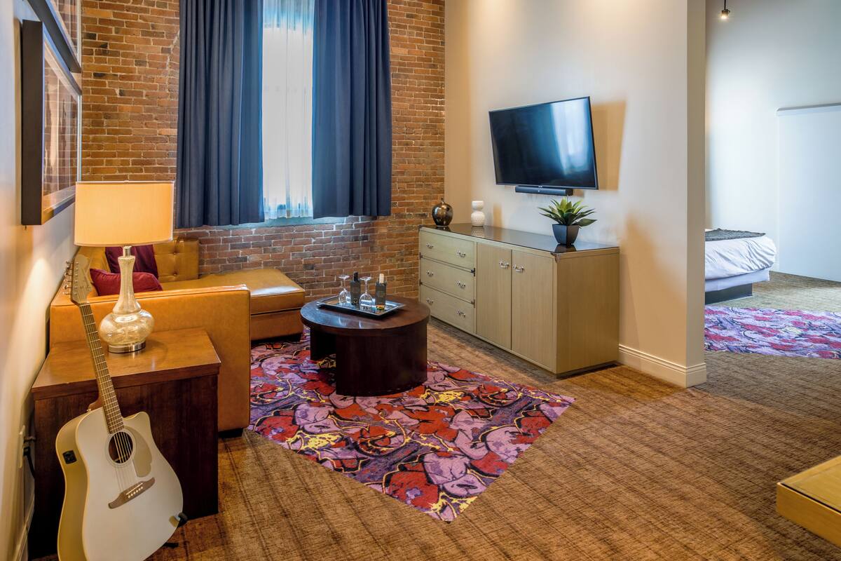 A modern living room with a brick wall, a flat-screen TV, a sofa, a coffee table, and a patterned rug.