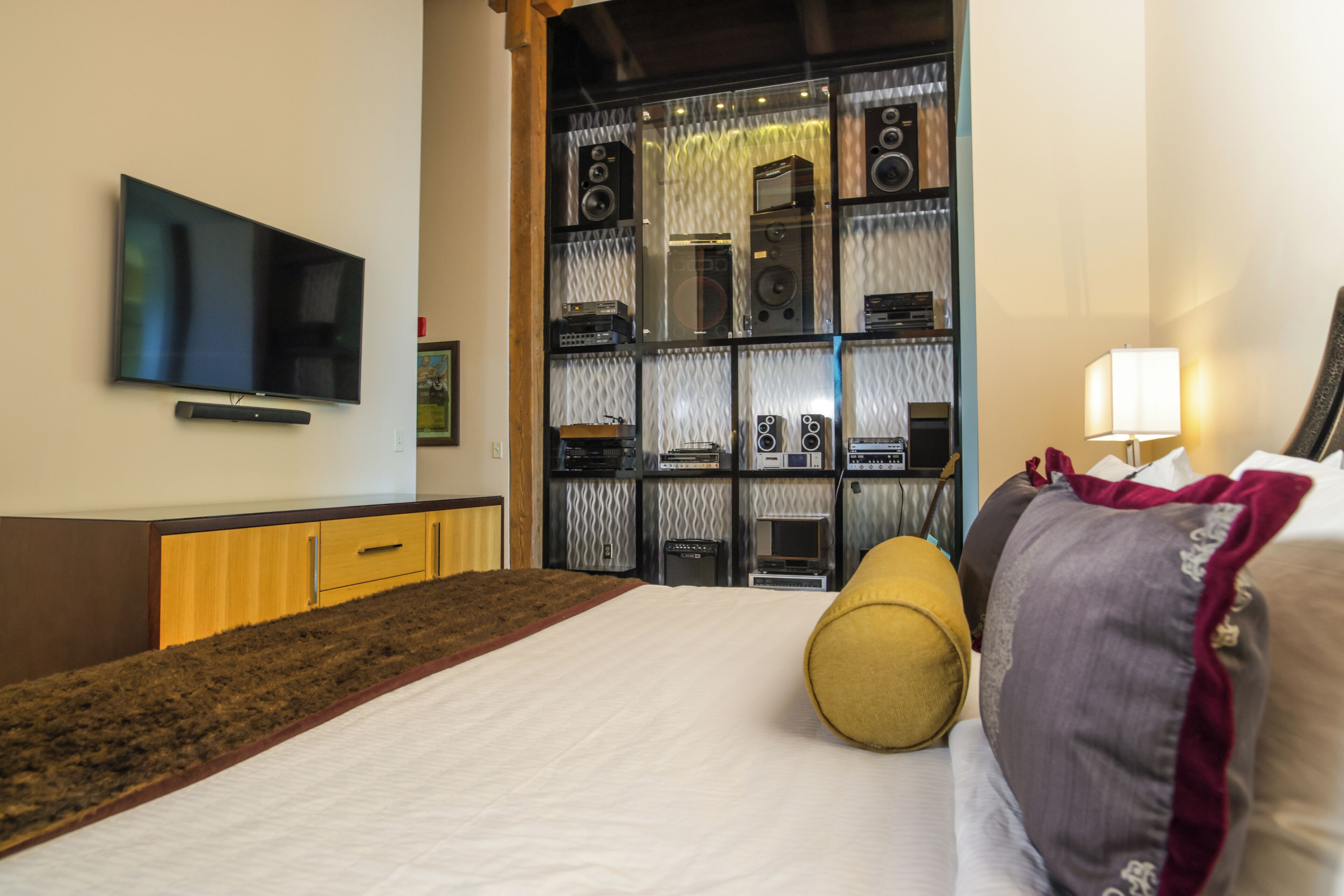 A hotel room with a bed, a television mounted on the wall, a sound system, and a lamp.